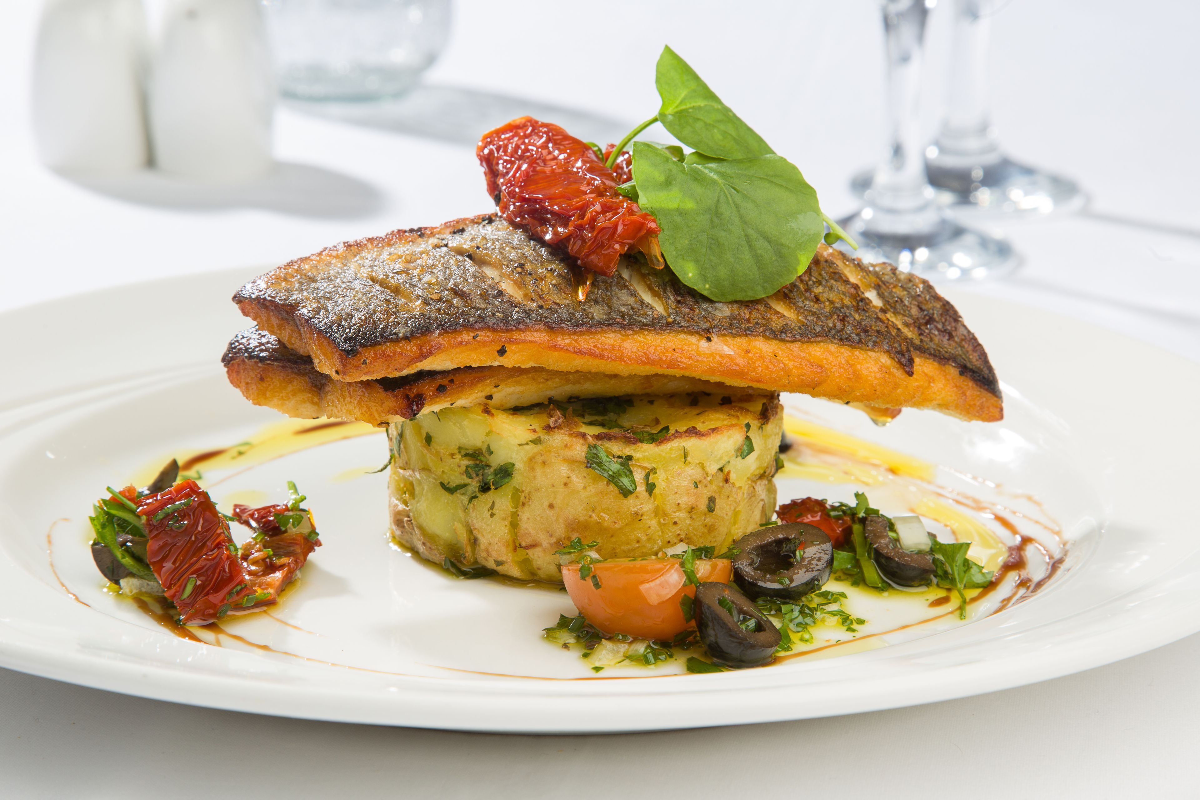 A plate of food with a fish, vegetables, and a garnish.