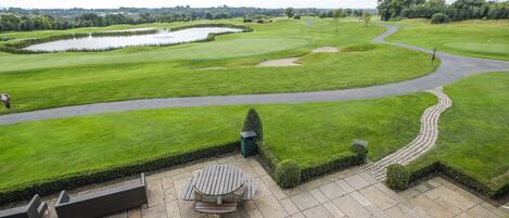 A golf course with a pond, a winding path, and a seating area with benches and a table.