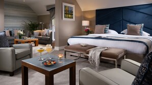 Una habitación de hotel moderna con una cama grande, un sofá, una mesa de centro con bebidas y un cuadro en la pared.