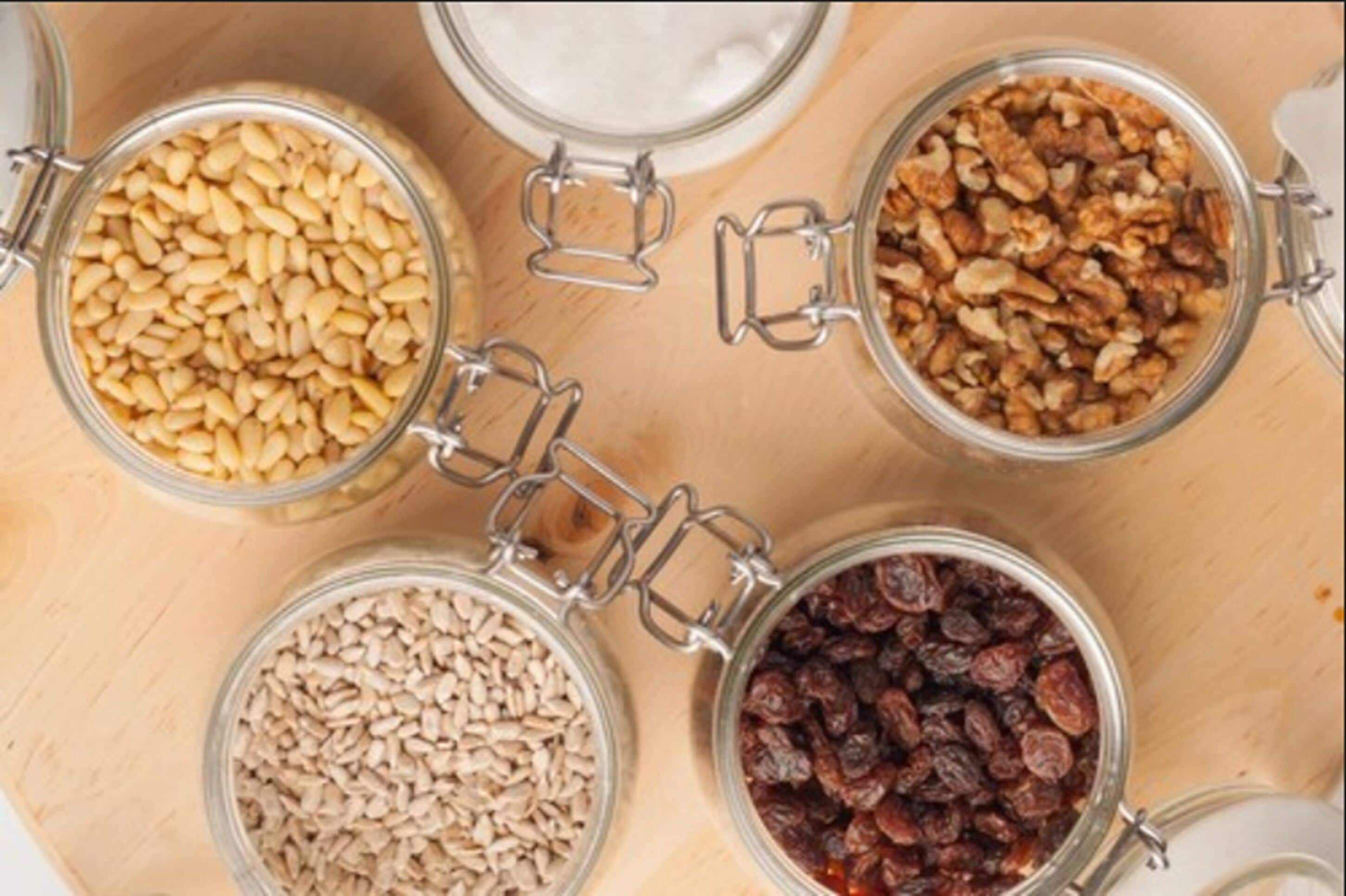 Four glass jars with metal clasps containing different types of nuts and seeds.