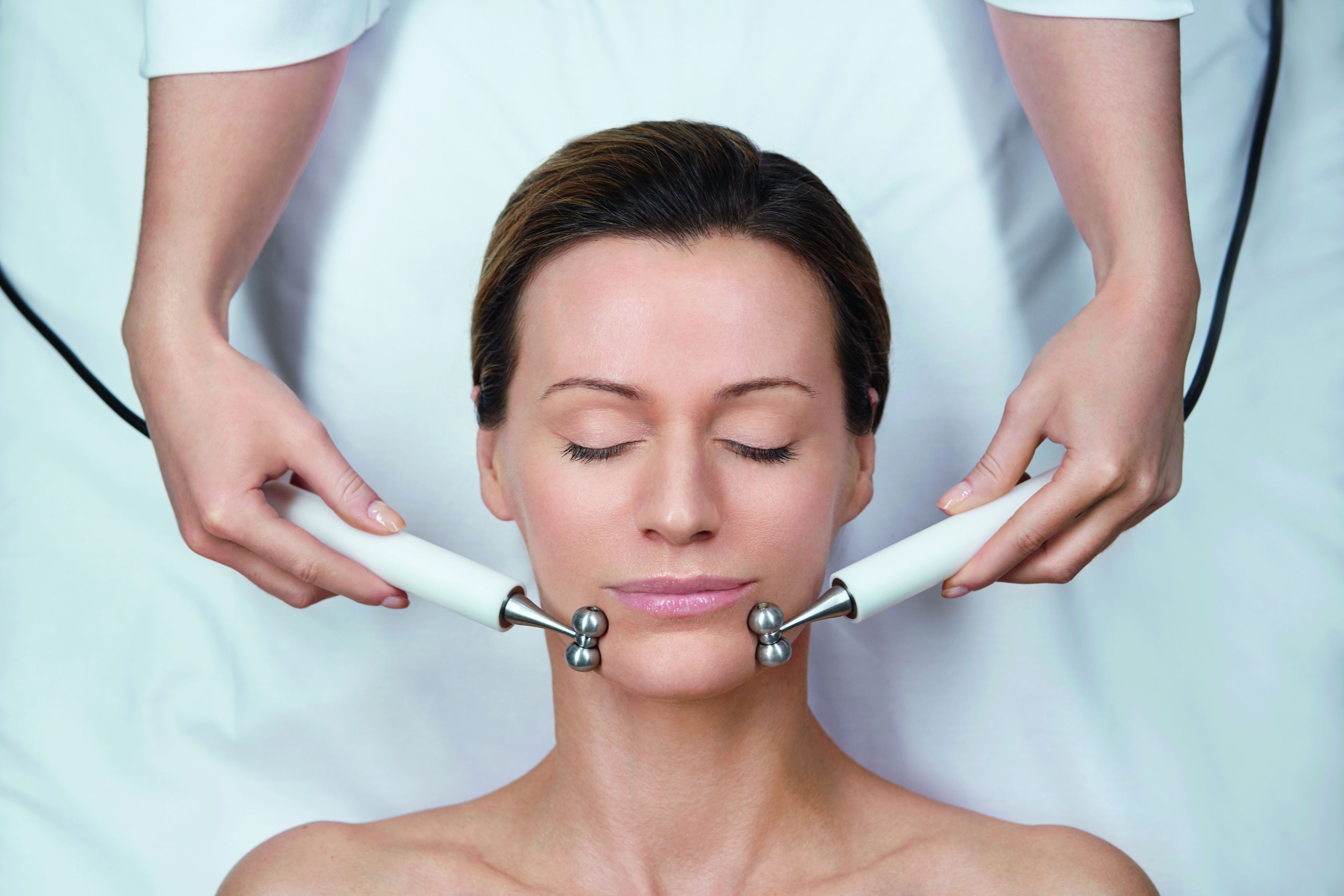 A person receiving a facial treatment with a device held by two individuals.