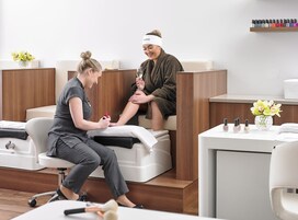 Um espaço de spa moderno com uma mesa de recepção, uma cadeira branca e um balcão de madeira.