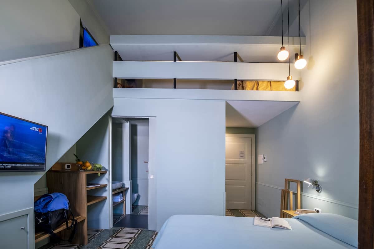 Habitación de hotel moderna con cama, televisión, escritorio y una escalera que conduce a un nivel superior.