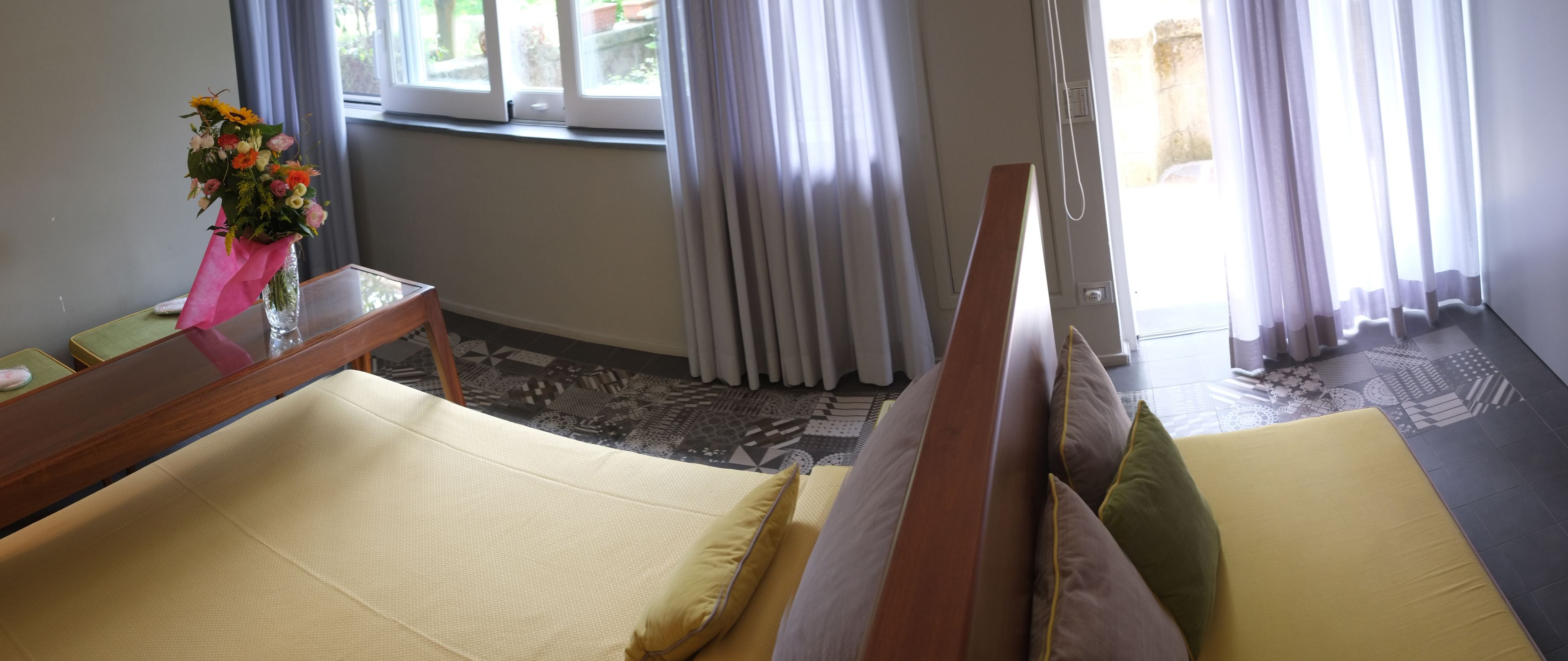 Une chambre d’hôtel avec un lit, une petite table sur laquelle est posé un vase de fleurs, et une vue sur l’extérieur par la fenêtre.