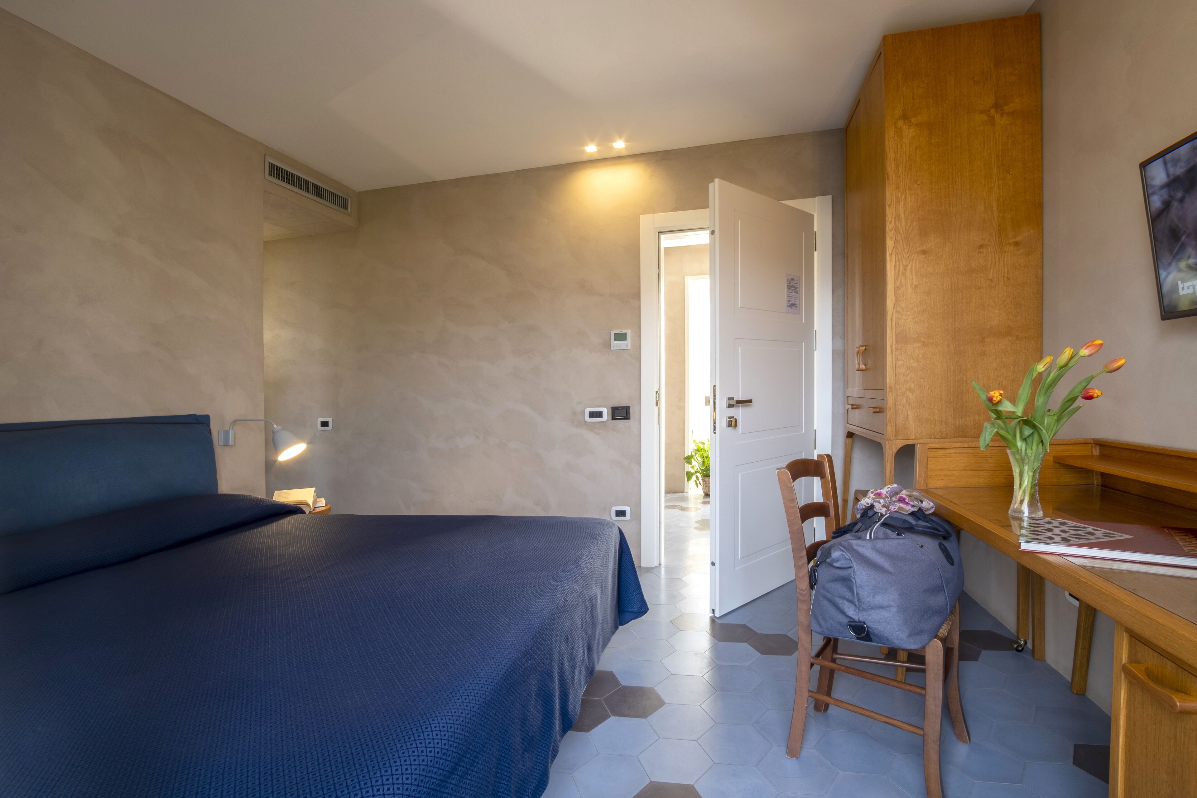 A bedroom with a bed, a desk, a chair, and a vase with flowers.