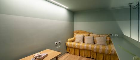 Una habitación pequeña y acogedora con una mesa de madera, un sofá amarillo y una pared verde claro.
