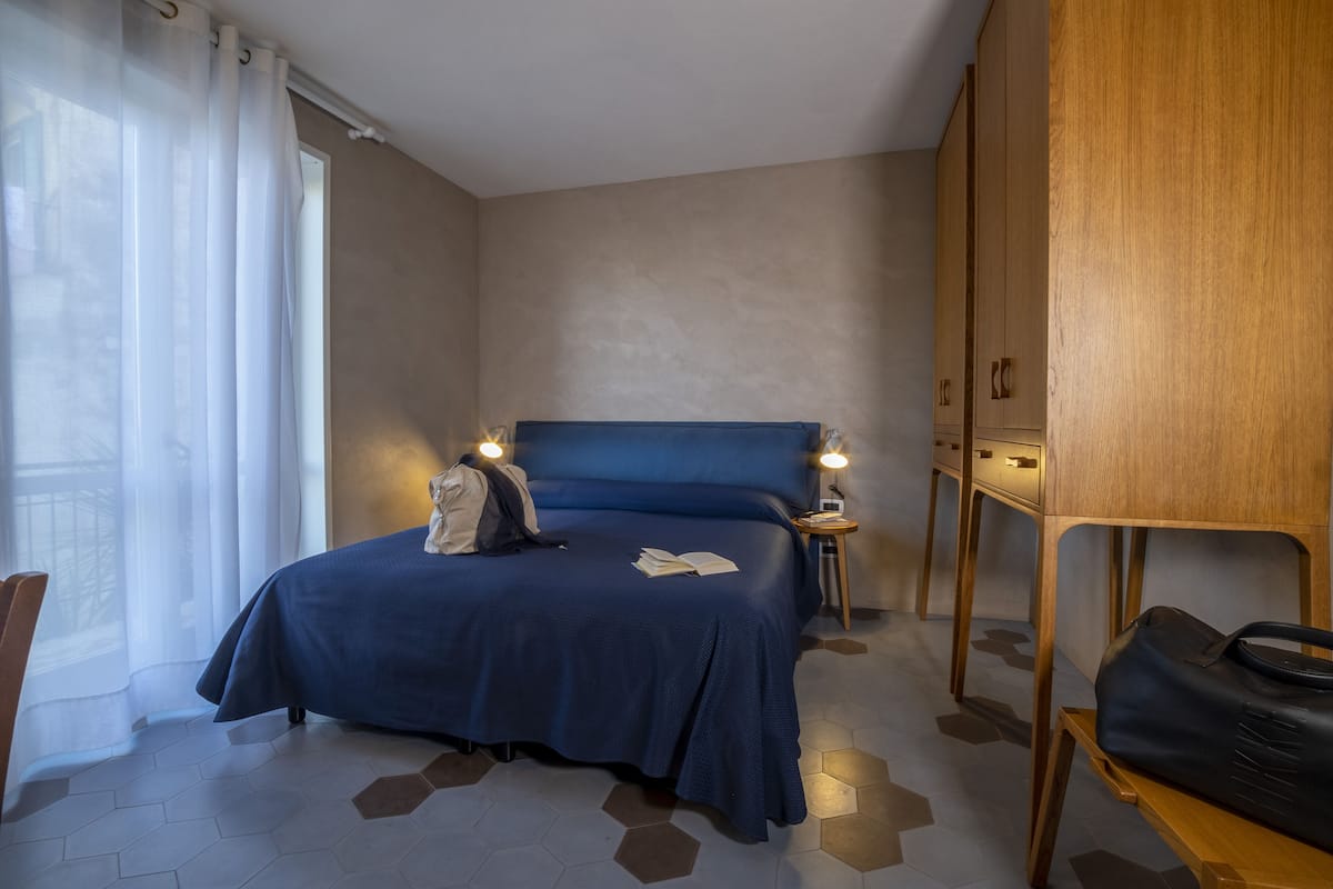 Una habitación de hotel con una cama grande, un armario de madera, una mesita pequeña y una silla.