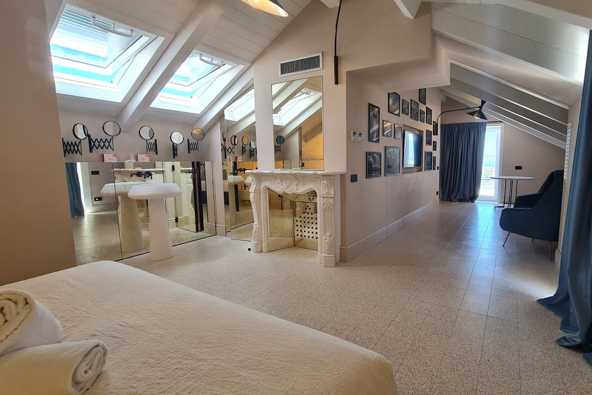 Una habitación amplia con una cama grande, un baño con espejo y un comedor con mesa y sillas.