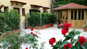 Un patio con plantas en macetas, un gazebo de madera y un edificio con ventanas y contraventanas.