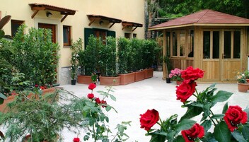 Un patio con plantas en macetas, un gazebo de madera y un edificio con ventanas y contraventanas.