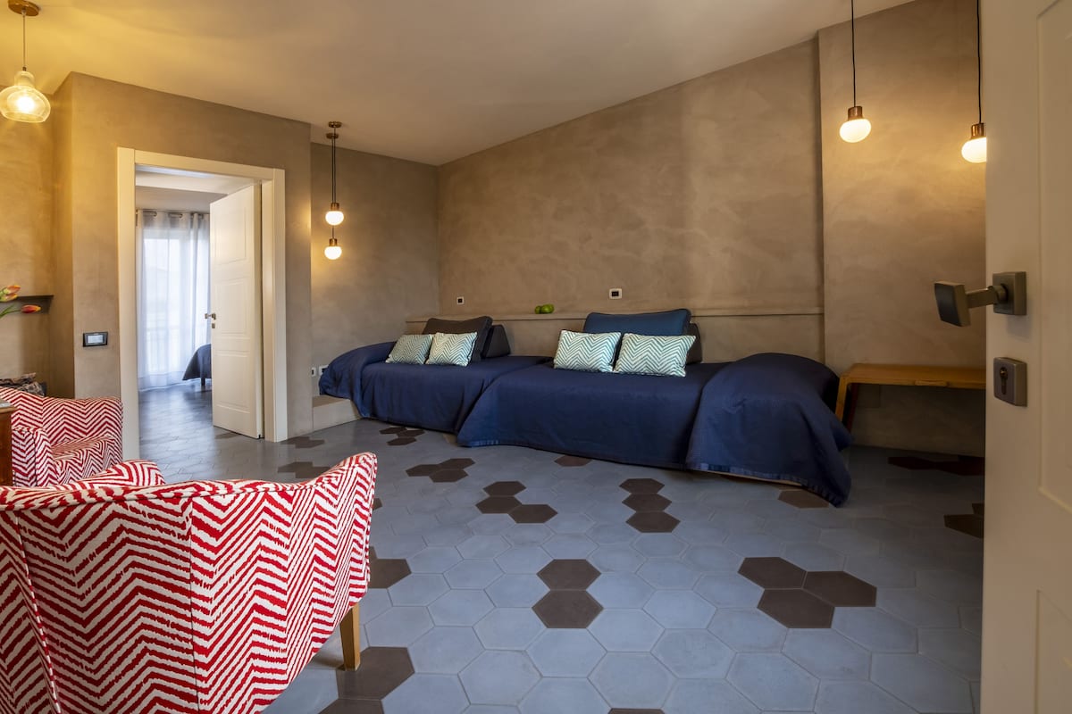 Un dormitorio moderno con una cama grande, dos mesitas de noche y una zona de estar con sillones estampados.