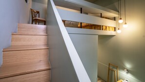 Una escalera moderna con escalones de madera y barandilla blanca, que conduce a un espacio tipo loft con lámparas colgantes.