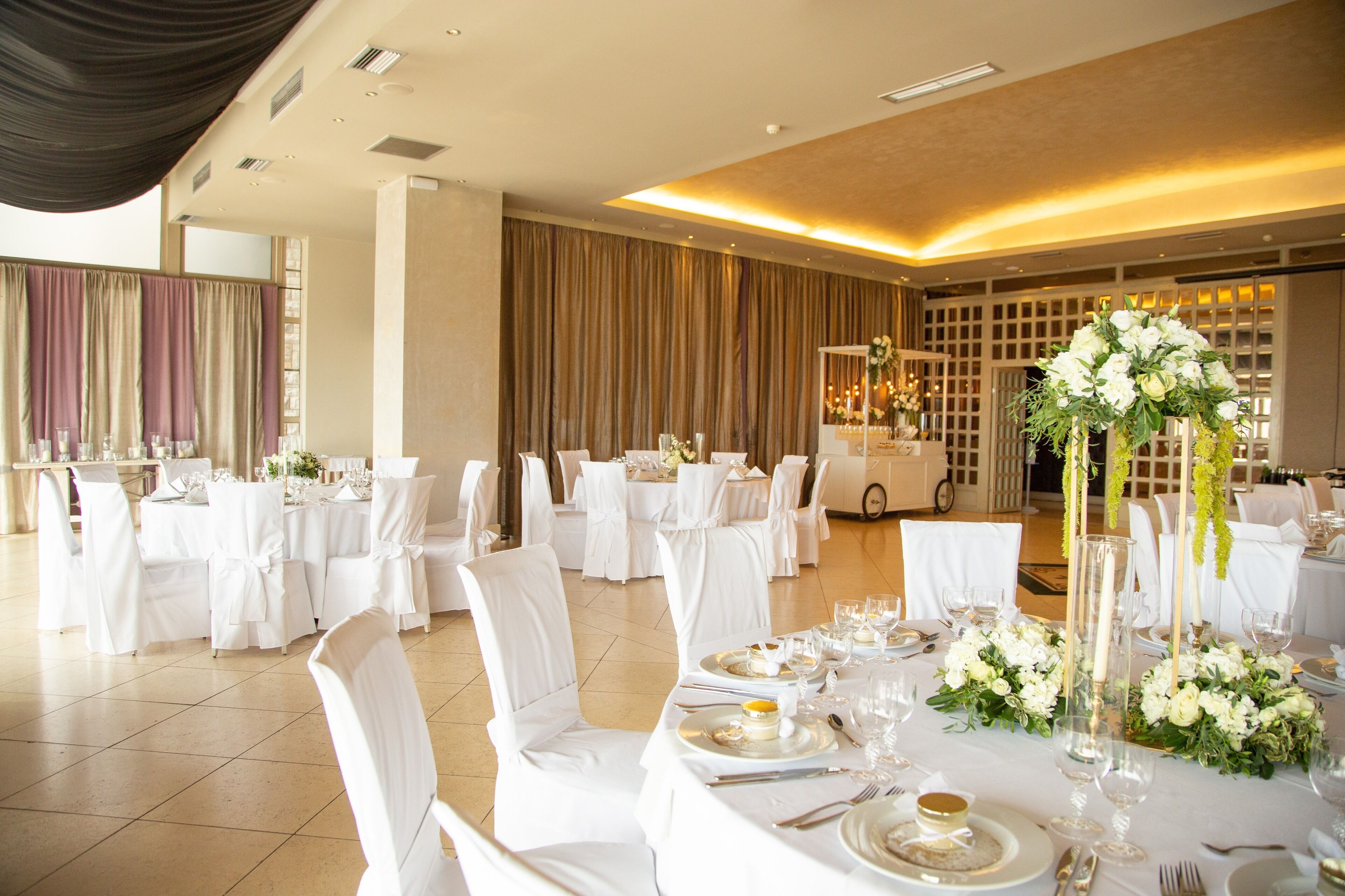 A banquet hall with round tables set for a formal event, featuring white tablecloths, chairs, and floral centerpieces.