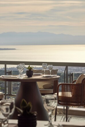 Una mesa de comedor con sillas y copas de vino, con vista a un cuerpo de agua y montañas distantes.
