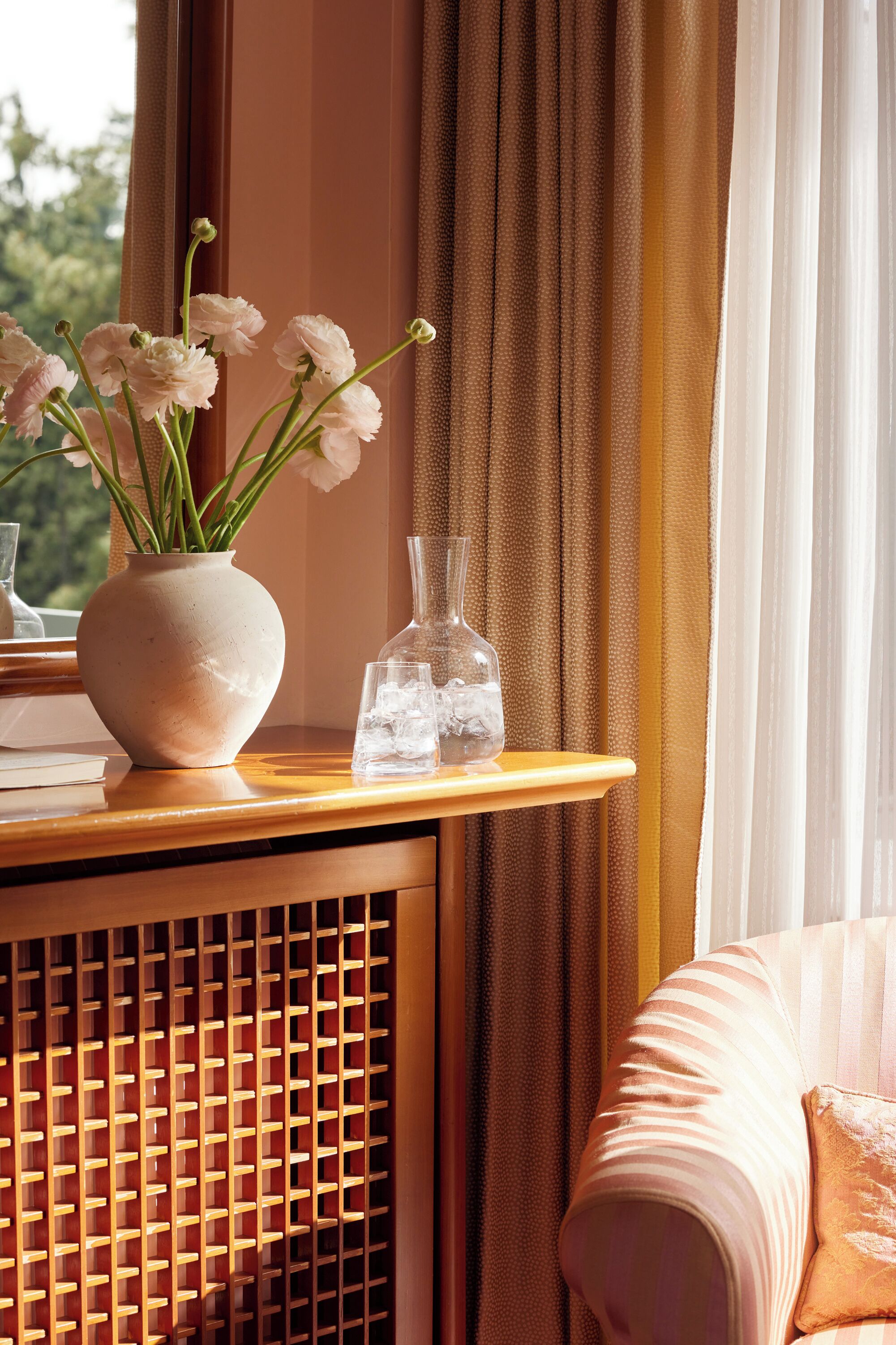 A room with a window, a vase with flowers, a glass bottle, and a wooden console table.