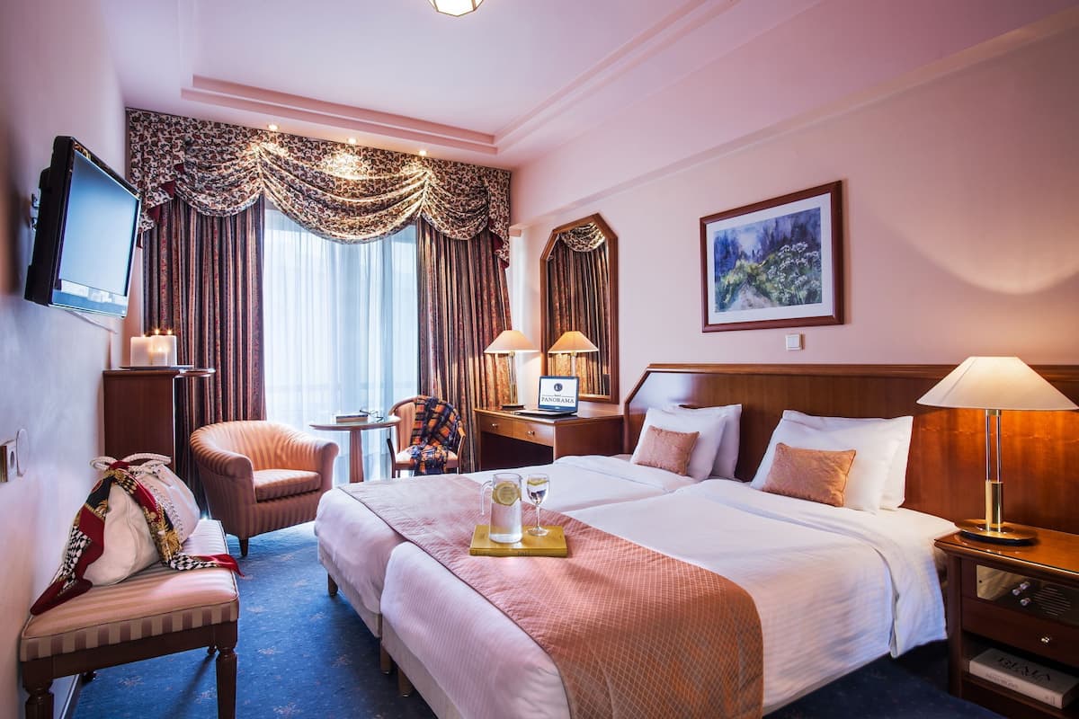 A hotel room with a bed, a desk, a chair, a TV, and a painting on the wall.
