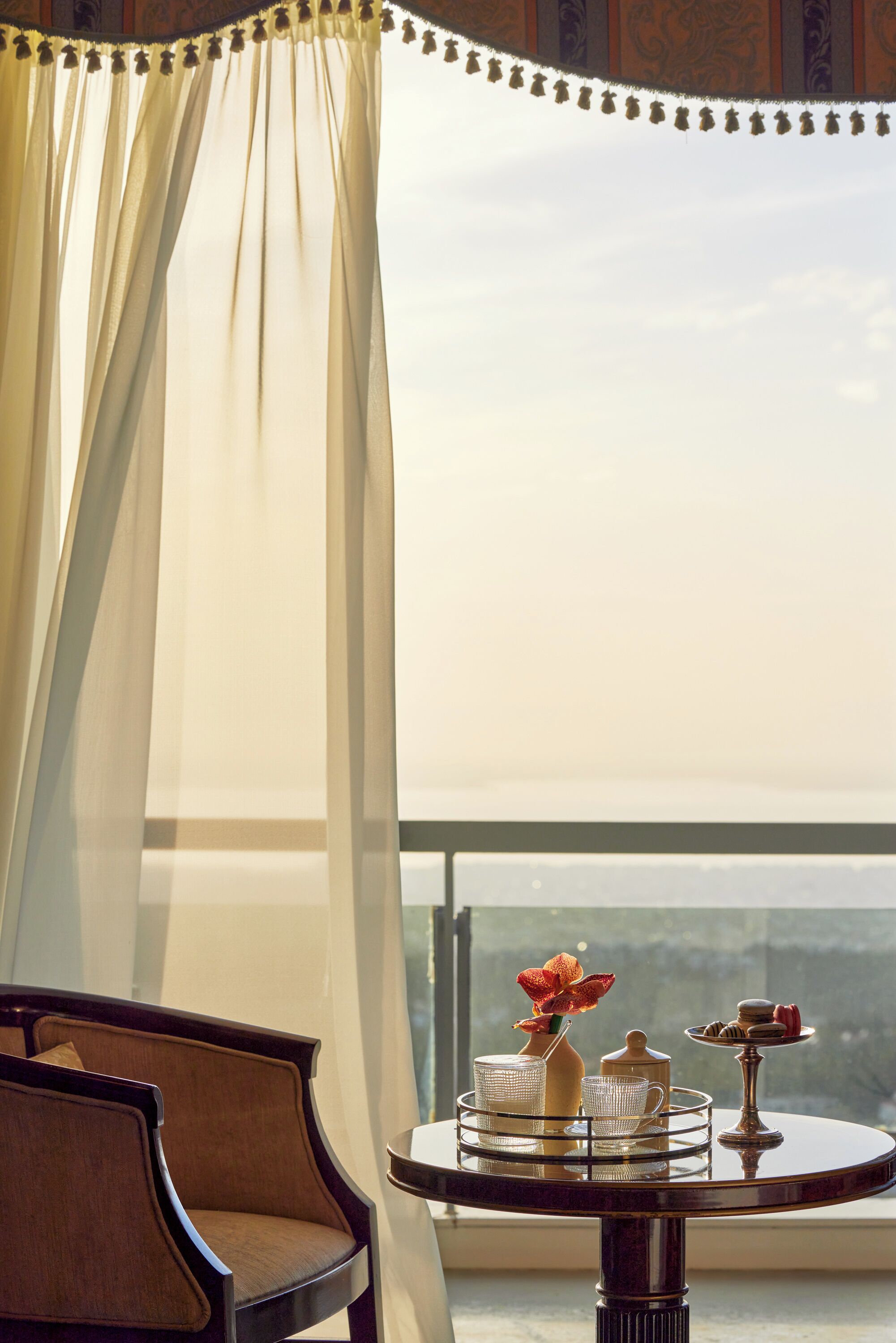 Una habitación con vista a la montaña, una mesa con un florero y tetera, y una silla.