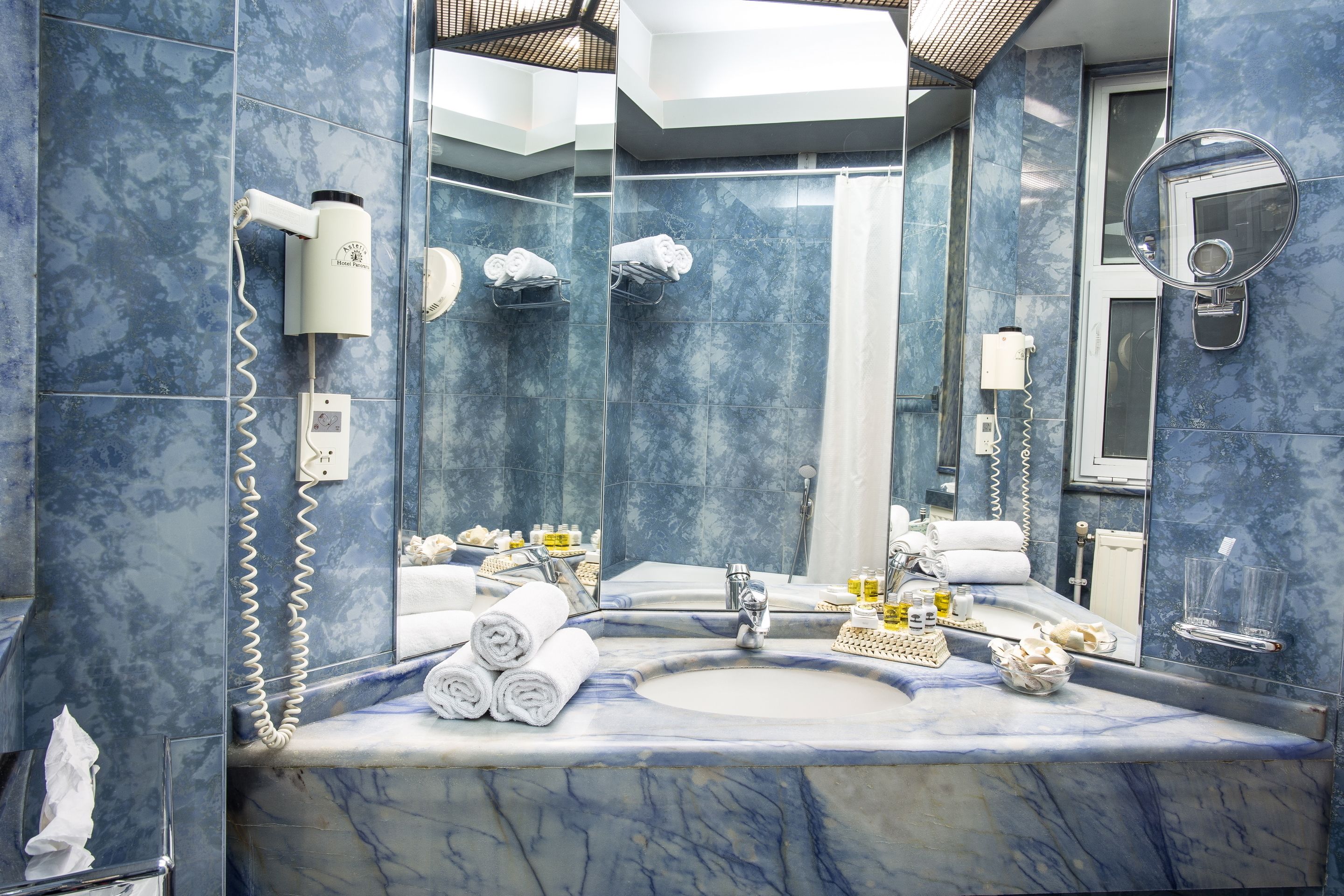 A bathroom with a marble sink, a large mirror, a hairdryer, and towels.