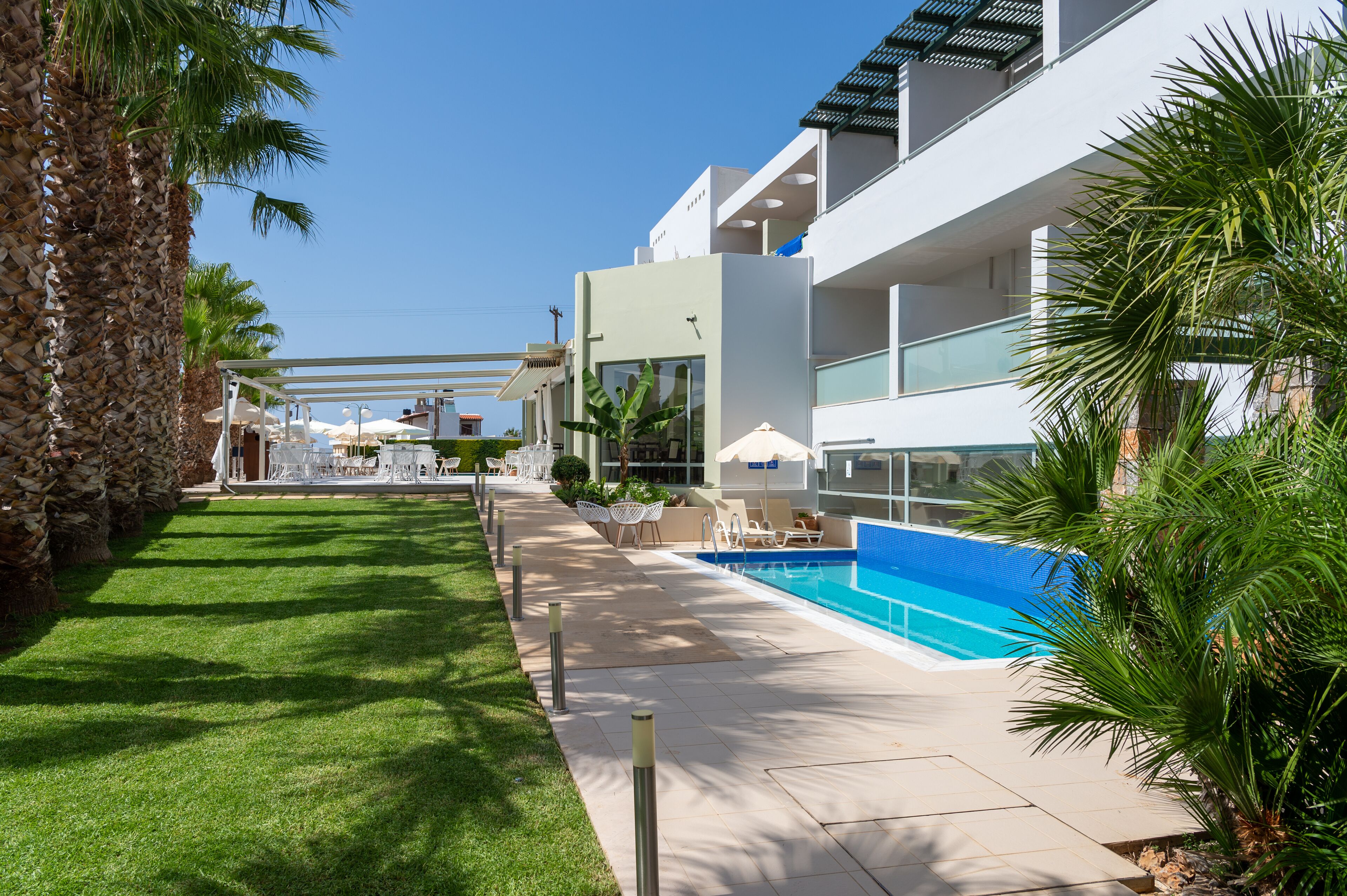 A modern hotel with a swimming pool, outdoor seating, and palm trees.