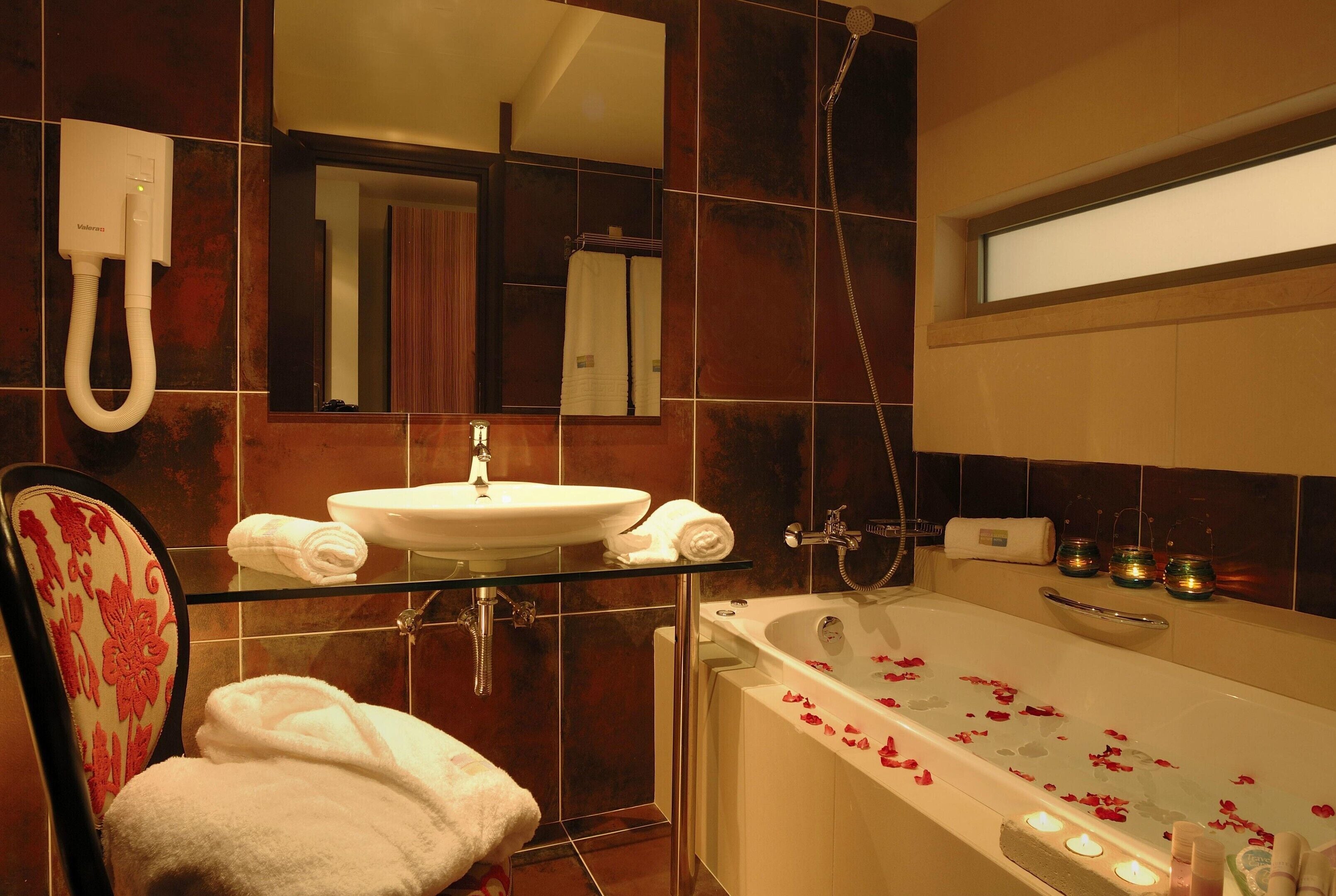 A bathroom with a glass shelf holding a white sink, a shower, and a bathtub with rose petals.