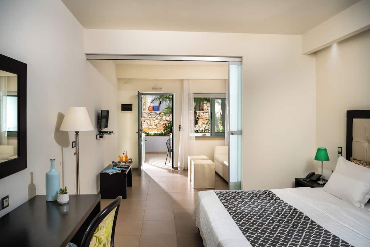 Ein modernes Hotelzimmer mit Bett, Nachttisch, Lampe und Blick auf den Balkon.