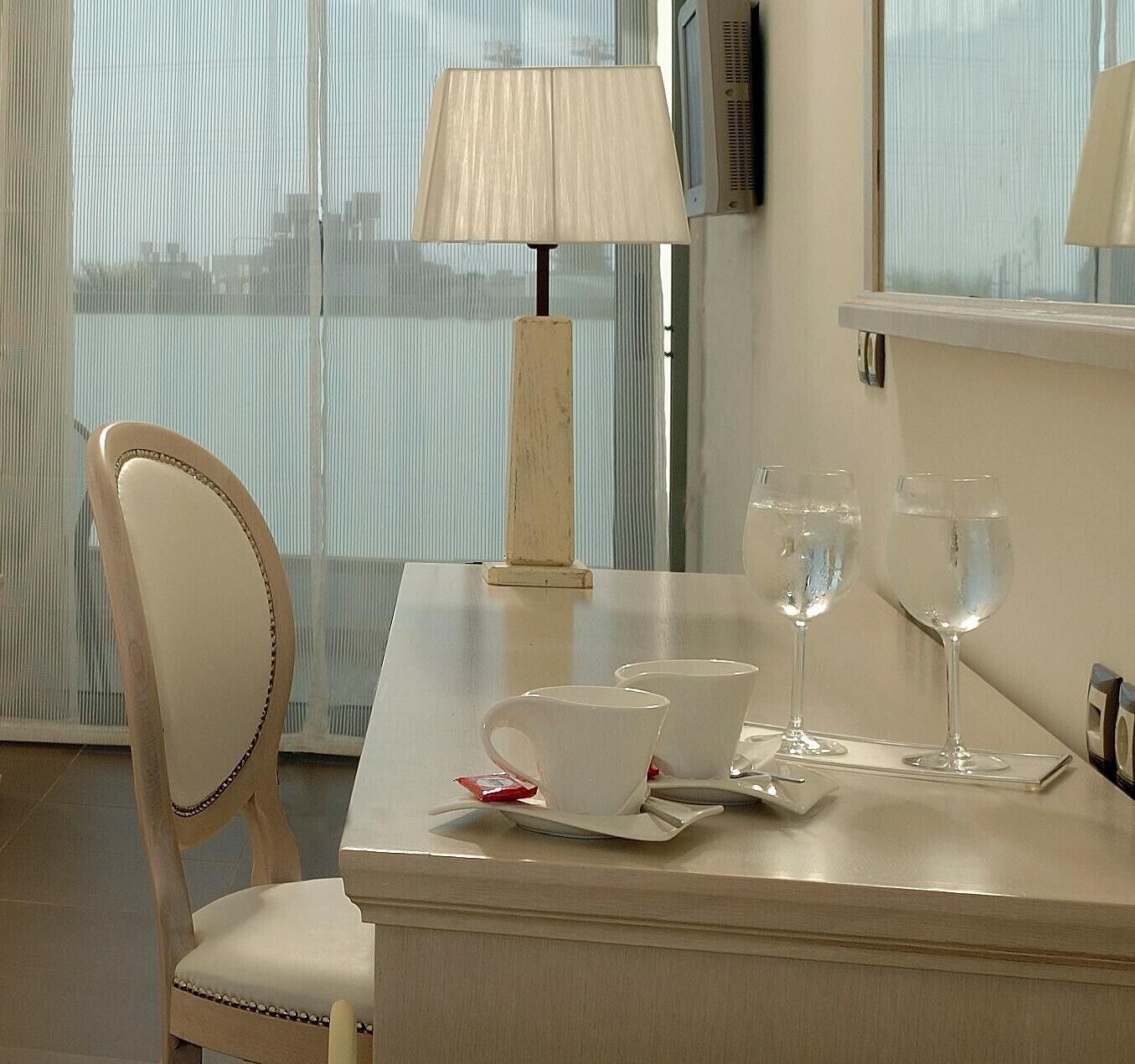 A hotel room with a table set for two, a chair, a lamp, and two glasses of water.