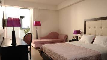 A hotel room with a bed, a desk, a chair, and a sofa.