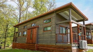 A wooden cabin with a porch, multiple windows, and a visible air conditioning unit. - Branson Cedars Resort (Ridgedale)