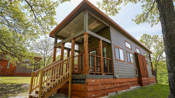 A cabin with a wooden deck, a staircase, and a large window. - Branson Cedars Resort (Ridgedale)