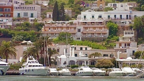 Un puerto deportivo con varios yates amarrados, rodeado de edificios con balcones y un paisaje de colinas.