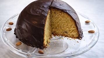A chocolate-covered cake on a glass cake stand with almonds around it.
