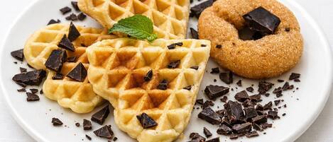 Three waffles and a donut on a plate with chocolate shavings and a mint leaf.