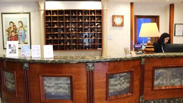 A reception desk with a wooden finish and a marble top, flanked by framed glass panels. Behind the desk is a shoe display and a wall clock.