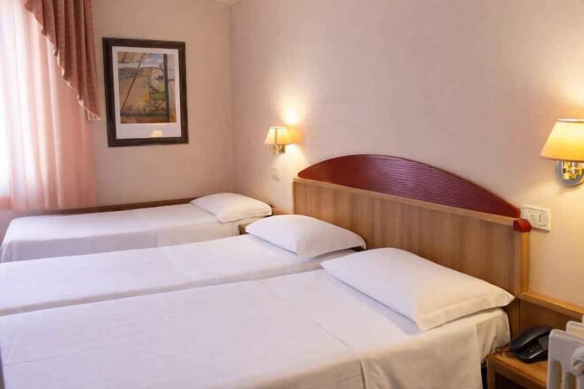 A hotel room with two single beds, a wooden headboard, a bedside lamp, a framed picture on the wall, and a telephone on the nightstand.