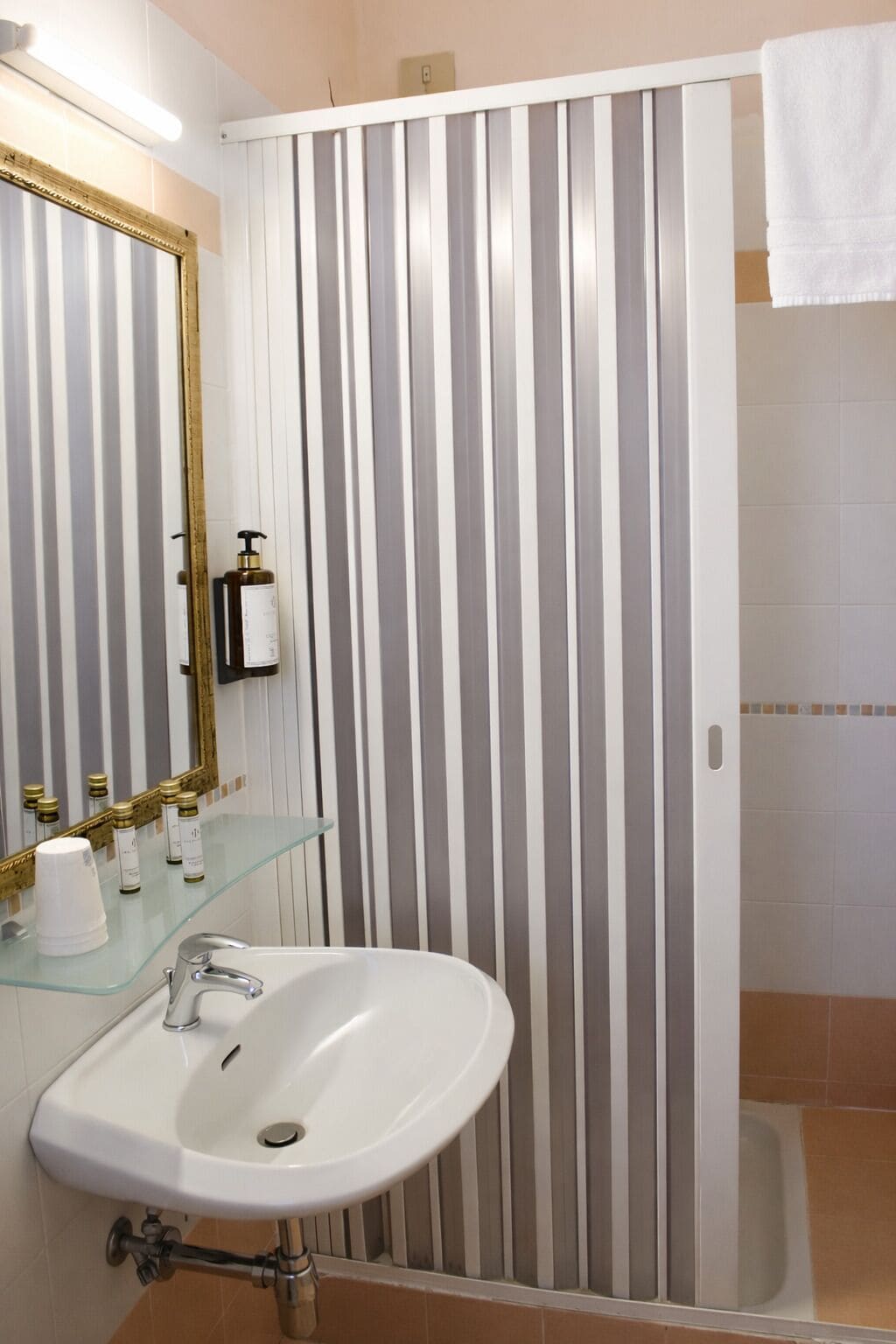 A bathroom with a white sink, a glass shelf with toiletries, a striped shower curtain, and a white towel hanging on the wall.