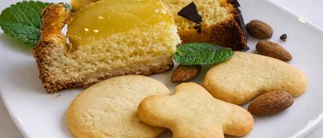 A plate with a slice of cake, cookies, almonds, and mint leaves.