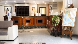 A hotel lobby with a reception desk, a sofa, a map on a stand, and a patterned carpet. - Phi Hotel Ambra (Pescara)