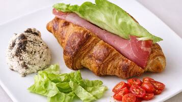 Un croissant con jamón y lechuga, una porción de morcilla y rodajas de tomate sobre un plato blanco.