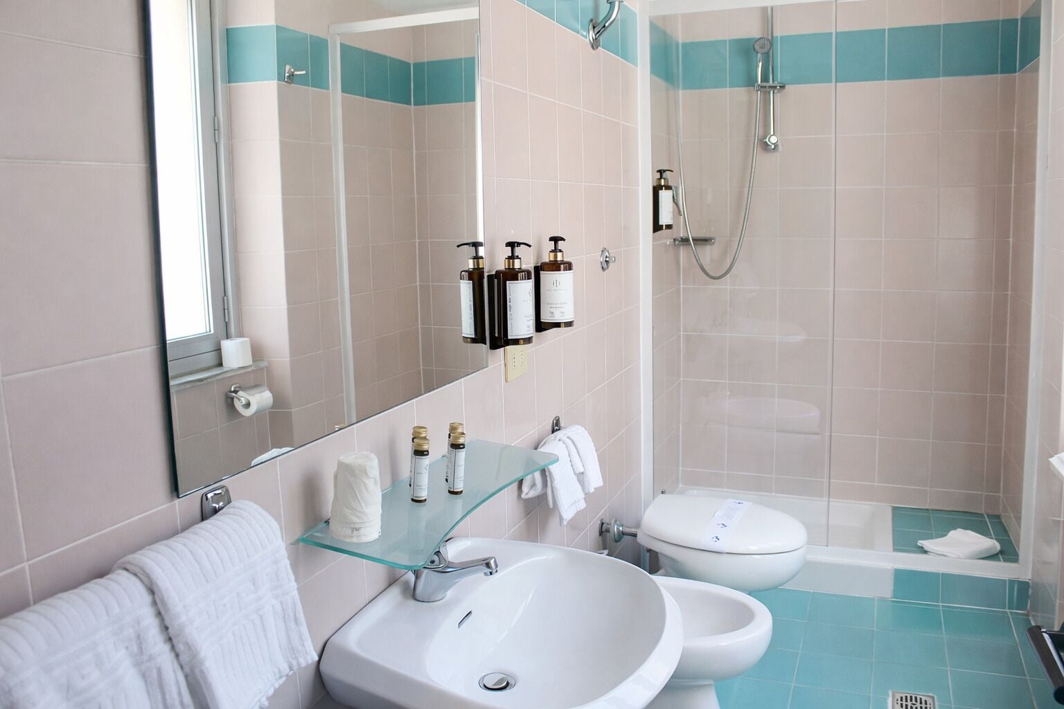 Ein modernes Badezimmer mit einer Glasablage für Pflegeartikel, einem weißen Waschbecken, einem Bidet und einer Duschkabine.