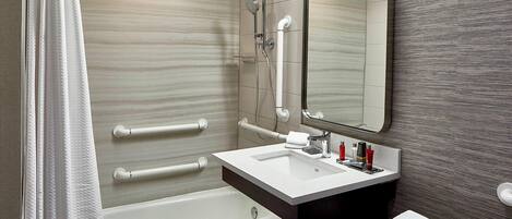 Un baño moderno con bañera, lavamanos con espejo y barras de apoyo.