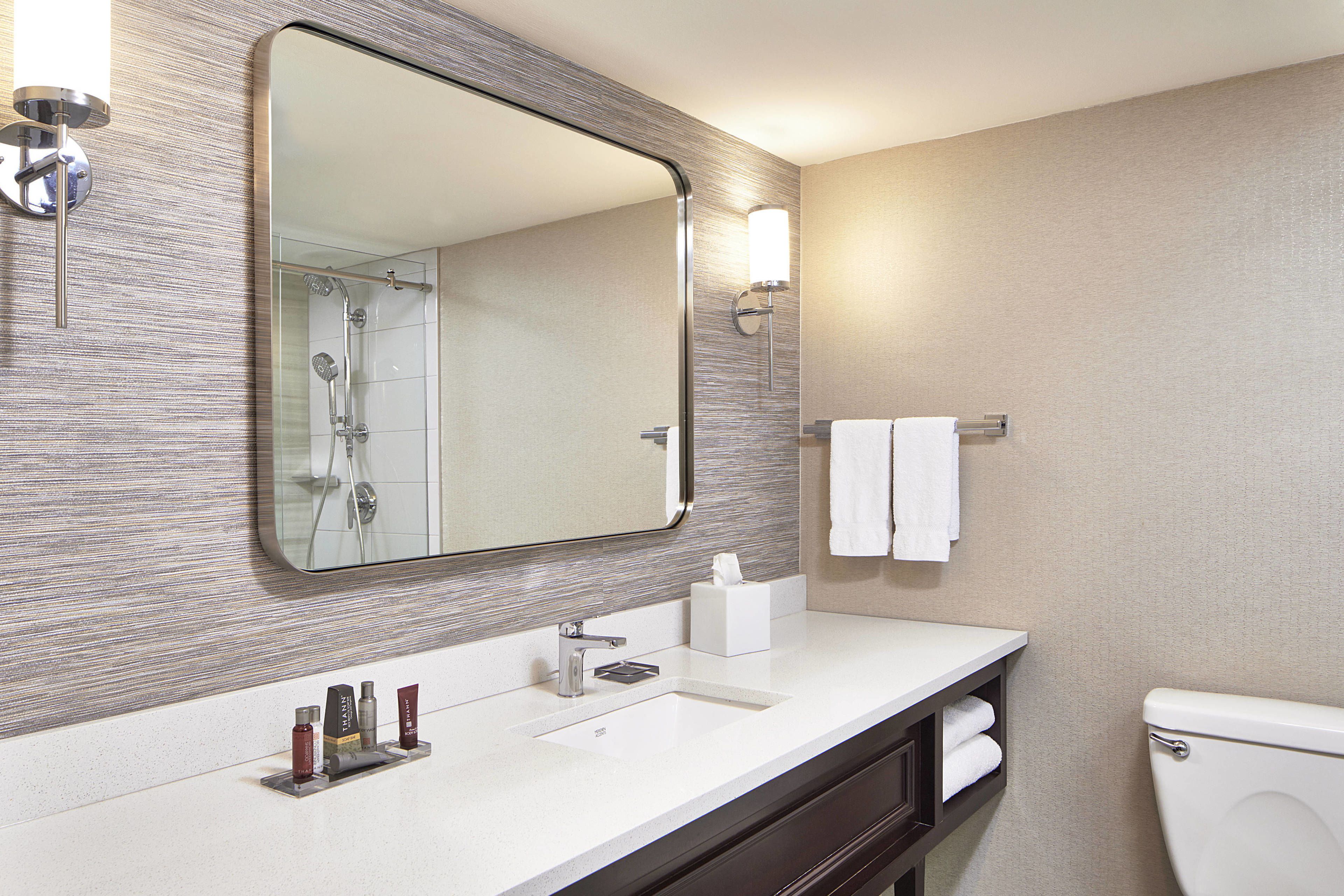 A modern bathroom with a large mirror, a sink with toiletries, a towel rack, and a toilet.