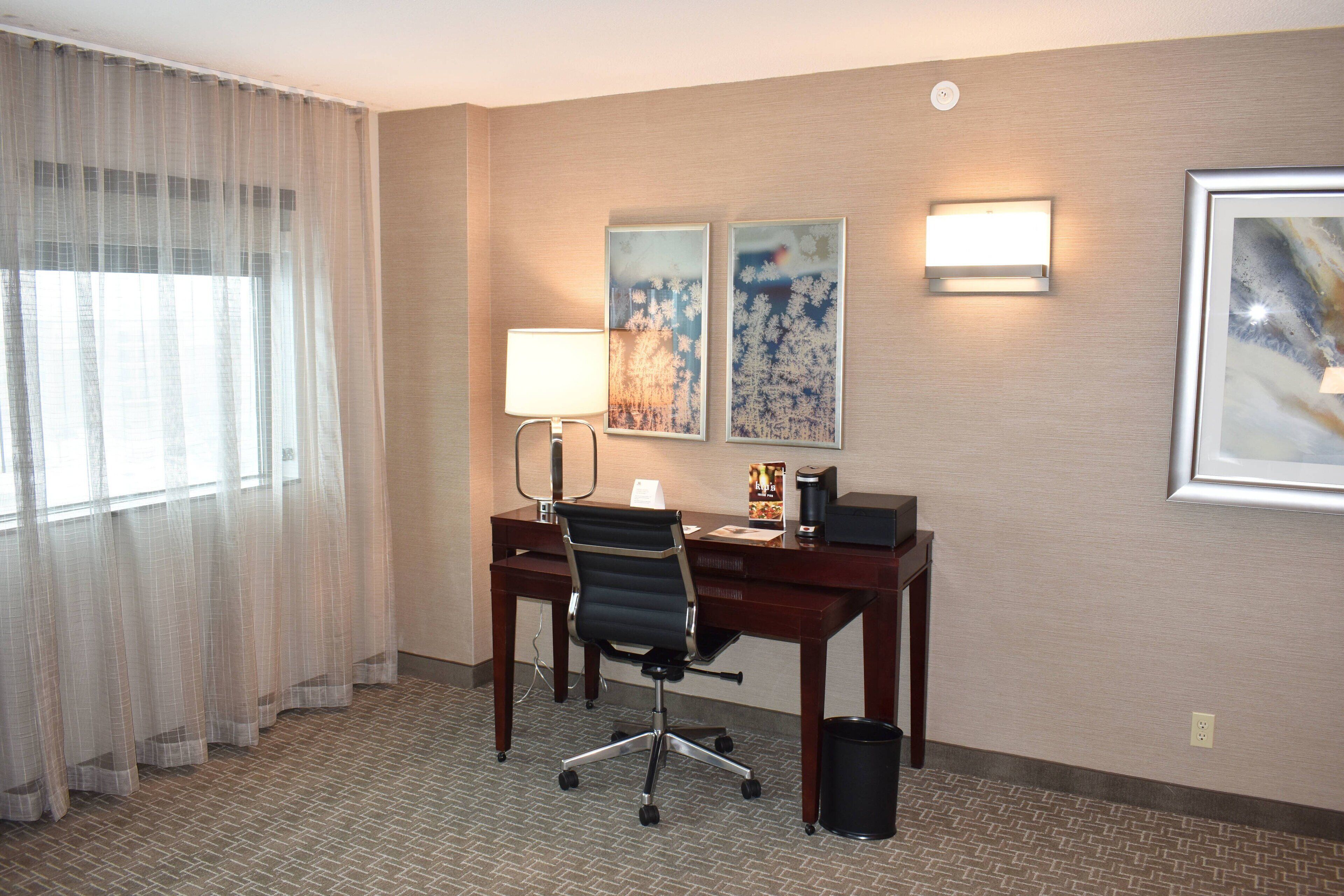 Une chambre d’hôtel équipée d’un bureau, d’une chaise, d’une lampe et d’une œuvre d’art au mur.