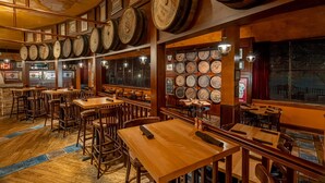 L’intérieur d’un restaurant est aménagé avec des tables et des chaises en bois, un mur composé de barils de vin et un espace bar.