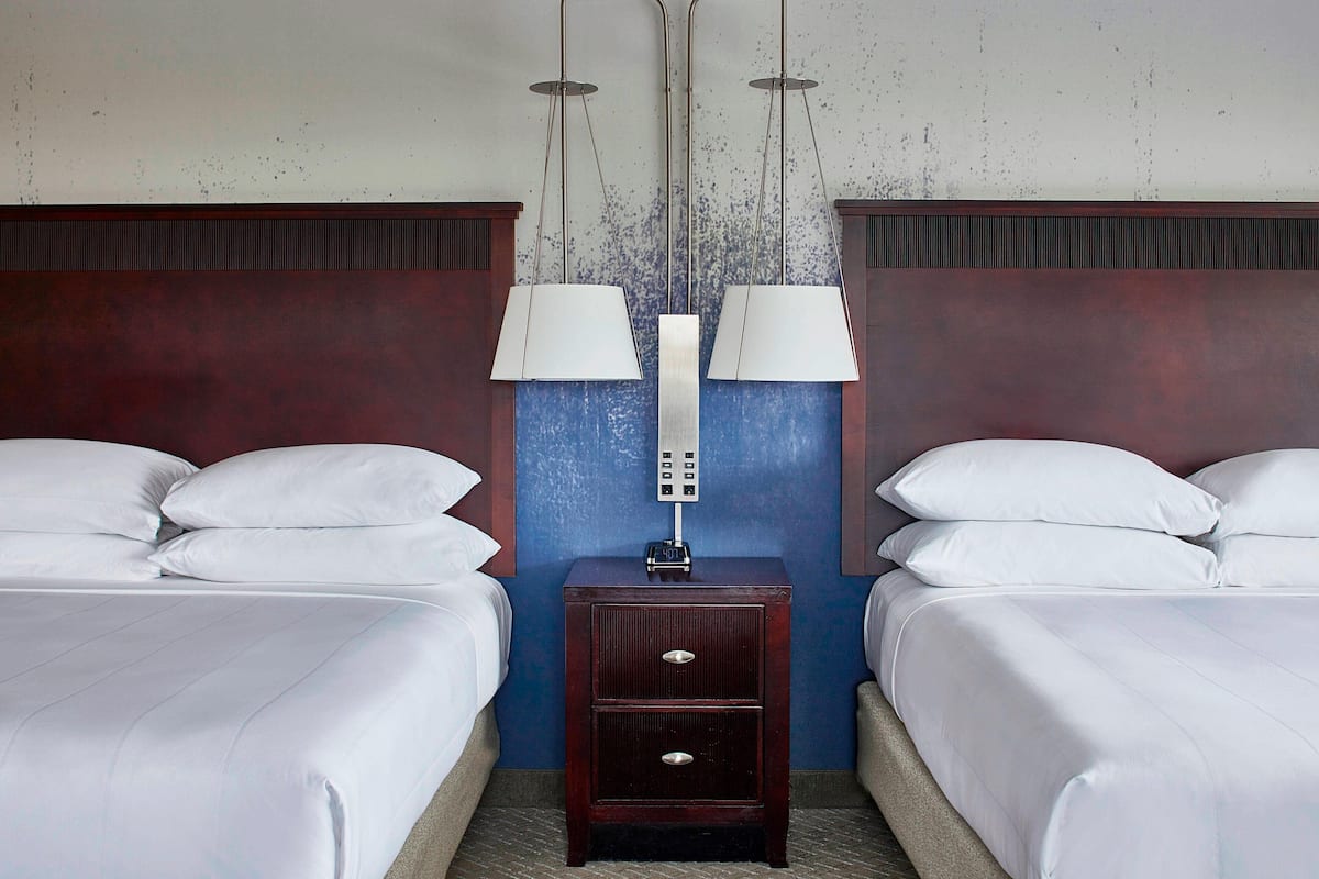 Habitació d'hotel amb dos llits, una tauleta de nit amb una làmpada i un panell de control a la paret.