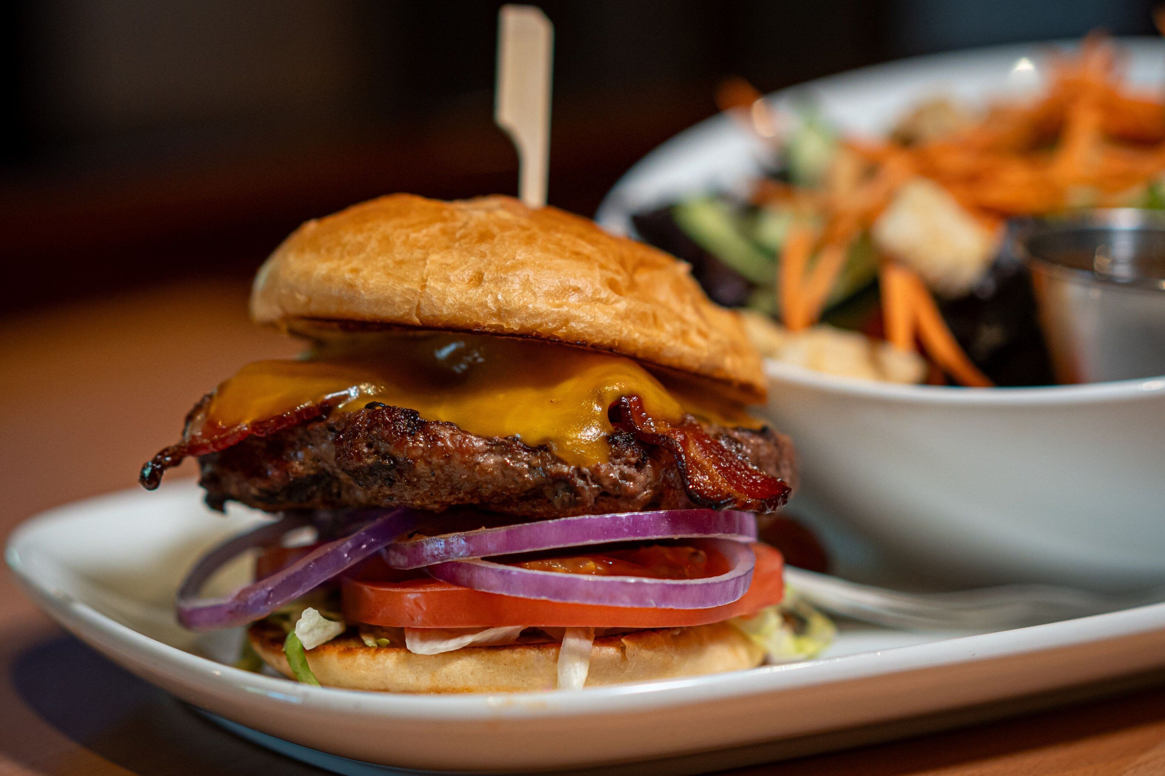 A close-up of a burger with a toasted bun, cheese, bacon, and vegetables.