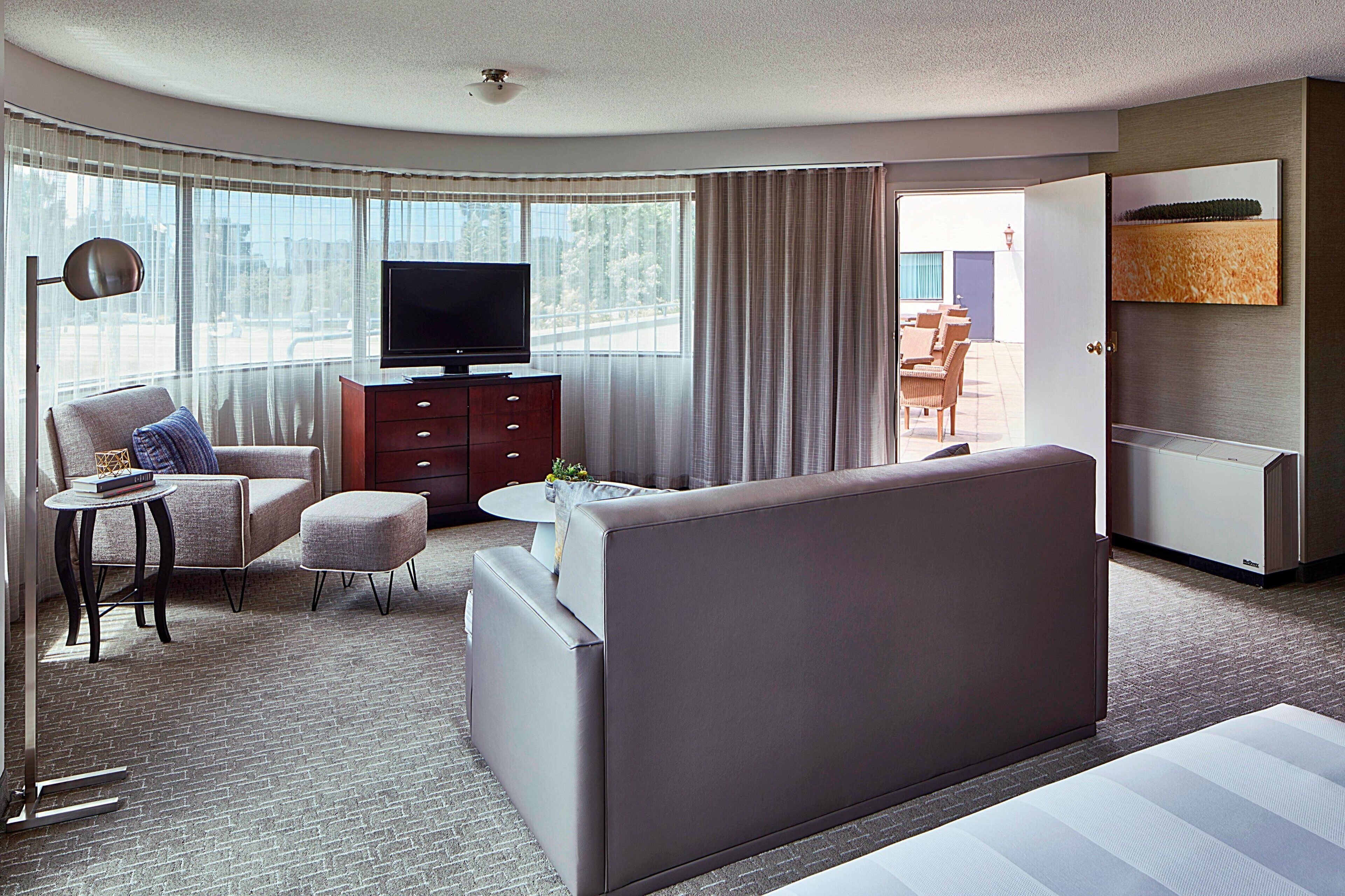 Una habitación de hotel moderna con sofá, sillón y televisor sobre un mueble de madera.