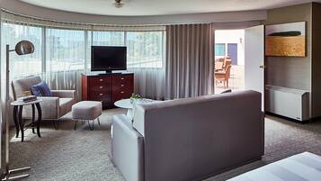 Una habitación de hotel moderna con sofá, sillón y televisor sobre un mueble de madera.