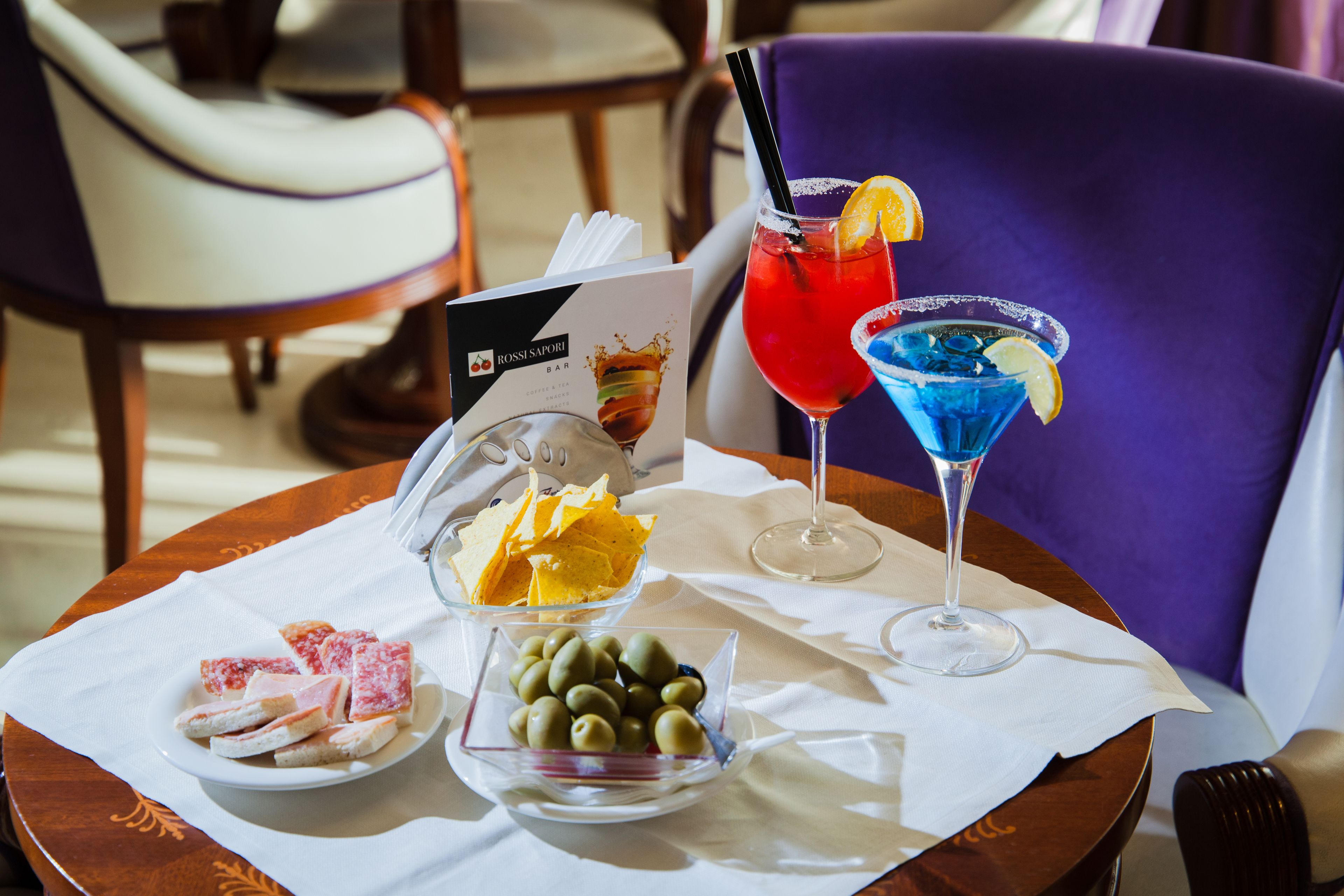 Une table avec un menu, une assiette de frites, un bol d’olives et deux cocktails.