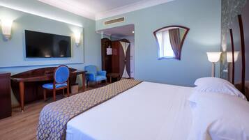 Ein Hotelzimmer mit einem Bett, einem Schreibtisch, einem Sessel, einem Fernseher und einem Vorhangfenster.