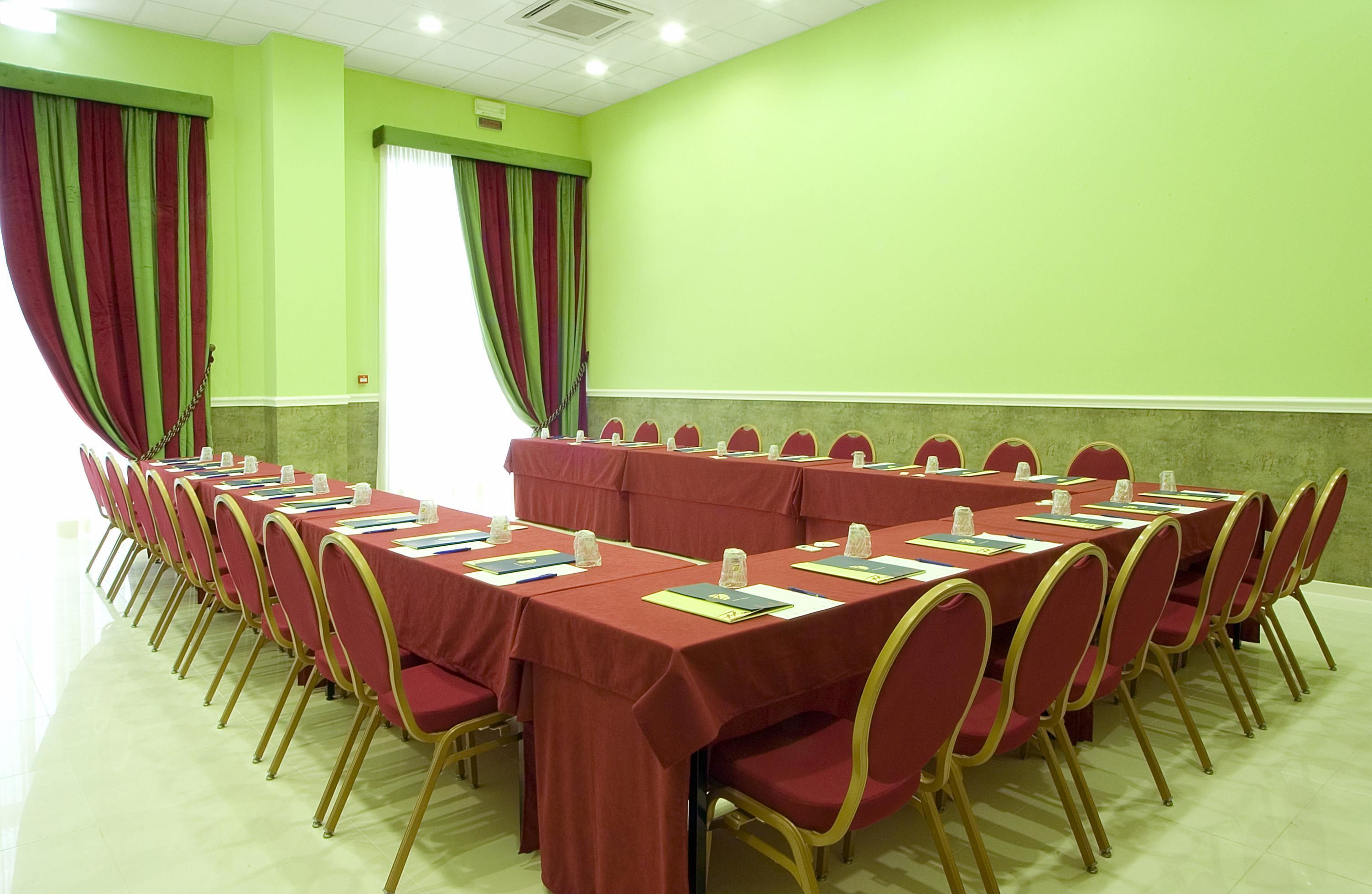 Un salón de conferencias con varias mesas y sillas, paredes verdes y cortinas.